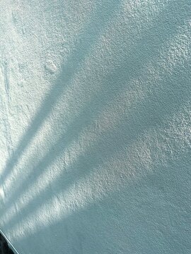 Sunlight casting long, parallel shadows on a textured light blue wall