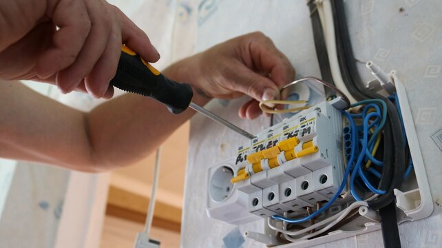 Maykop, Adygea, Russia &ndash; September 12, 2026: An electrician installs circuit breakers in a distribution board using a screwdriver. A close-up of the technician's hands connecting wires while repairing