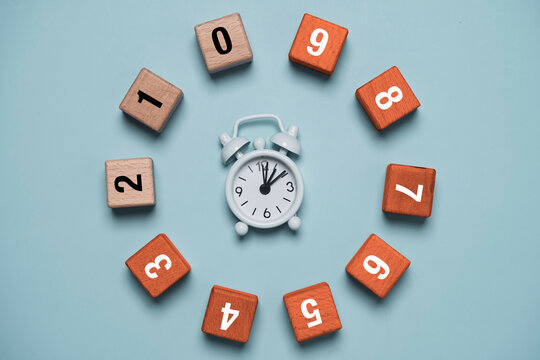 Time management concept with white alarm clock surrounded by numbered wooden blocks arranged in a circle symbolize countdown deadlines, project scheduling for productivity.