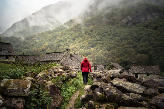 Woman hikes in misty Val Bavona toward traditional rustici in Ticino (Switzerland), ideal for outdoor travel