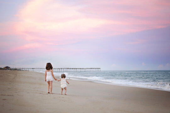 Two young sisters hold hands on the beach at sunset