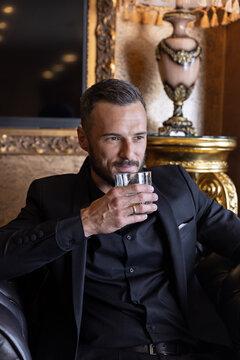 Handsome wealthy man sitting in leather armchair drinking whiskey