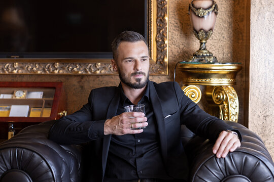 Successful elegant man in black suit relaxing in leather armchair