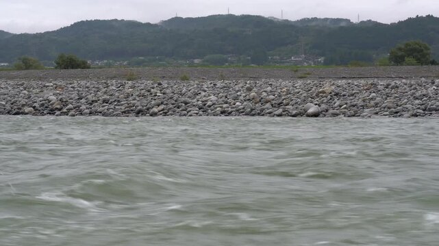 Swollen river running along a cobble bank below misty hills