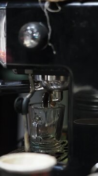 Black coffee machine pours dark brew into glass cup