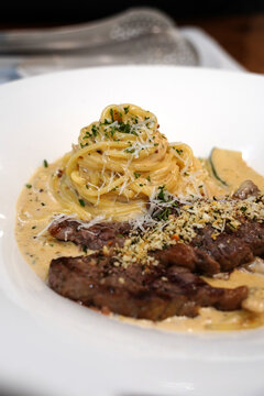 Creamy pasta topped with tender grilled beef steak slice on a white plate