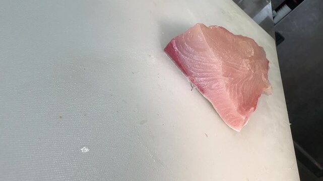 Japanese chef slicing fresh amberjack kanpachi sashimi with a knife on a white cutting board, izakaya kitchen, Japan