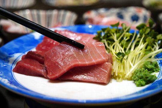 Black chopsticks picking up a fresh raw tuna sashimi slice from a plate