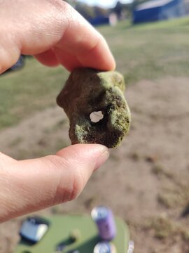 Close-up of a weathered stone with a natural hole, hag stone, held between fingers outdoors 