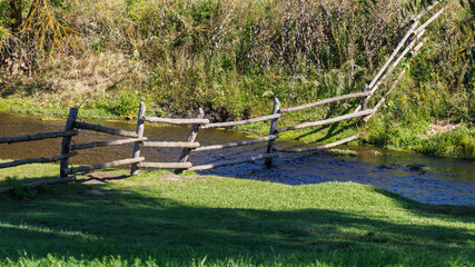 Obraz premium Rustic wooden fence leans over shallow stream