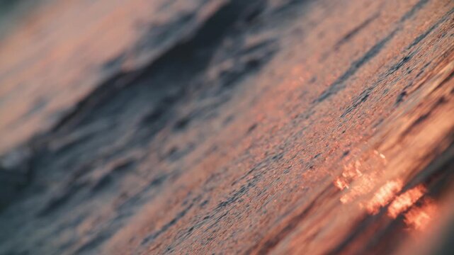 A diagonal band of blue surf borders copper sunset reflections on wet sand. Warm and cool colors form a dreamlike slow motion shoreline at Koh Kood, Thailand.