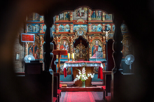 Interior of the historic wooden Church of St. Procopius and St. Barbara in Kuncice pod Ondrejnikem, Czech Republic, featuring a richly decorated altar with colorful religious icons.