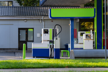 Fuel dispensers with hanging delivery hoses stand beneath a service station canopy, showing pump islands and payment equipment for retail vehicle refueling © K