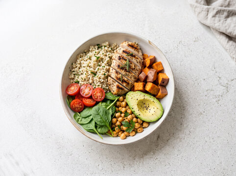 Healthy meal bowl with grilled chicken, quinoa, vegetables, and chickpeas on a light table