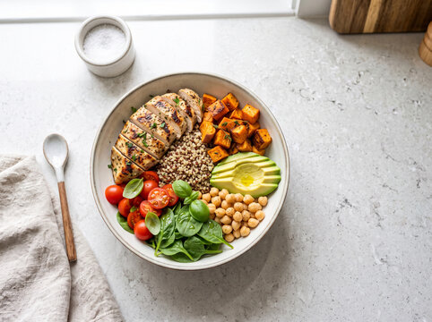 Healthy meal bowl with grilled chicken, vegetables, and grains on a kitchen counter