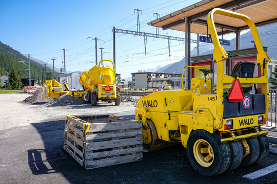 BEVER SWITZERLAND - AUGUST 15 2021: Yellow Walo road roller and machinery working on railway station infrastructure site under sunny blue sky with mountains.