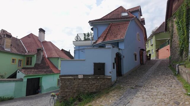 Pastel historic houses and tiled rooftops along a cobblestone street in Sighisoara Romania