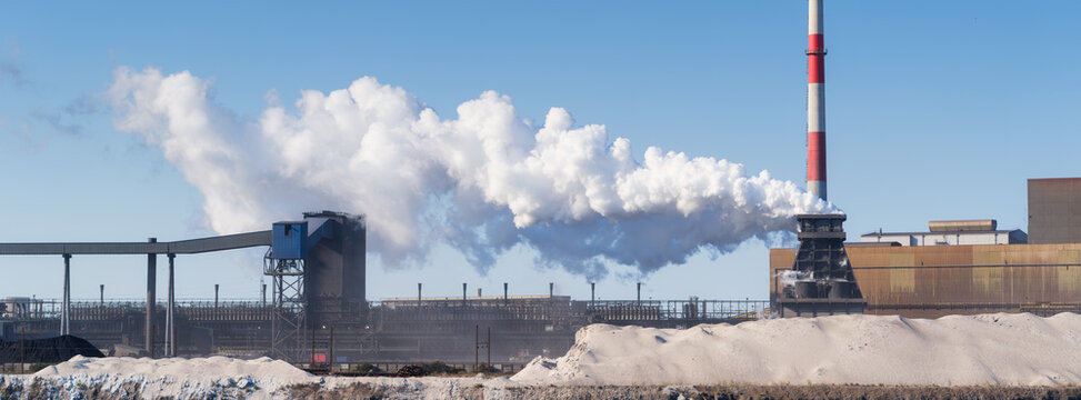 Heavy industrial steel plant with smoke emissions into the atmosphere. Wide panoramic view. Metallurgical manufacturing process and environmental air pollution.