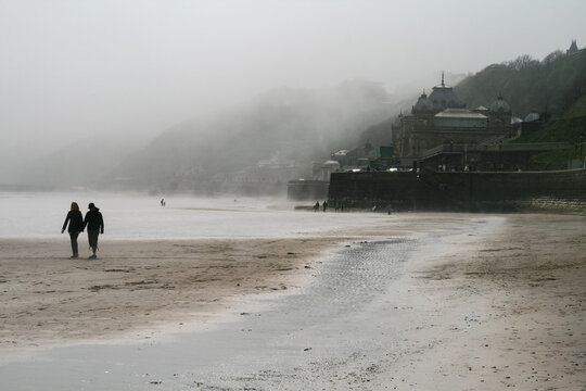 People walking along Scarborough beach with the Scarborough Spa visible in the background