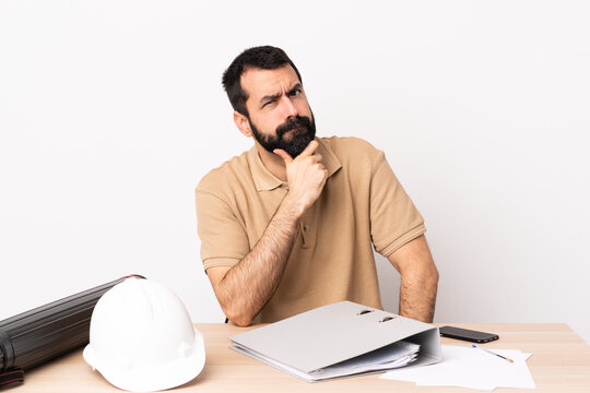 Caucasian architect man with beard in a table having doubts.