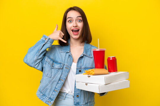 Young Ukrainian woman holding fast food isolated on yellow background making phone gesture. Call me back sign