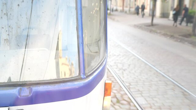 An older tram cab with windshield wipers travels alongside street embedded rails and pedestrians, illustrating shared urban transport space and passenger rail service