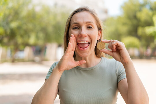 Young blonde woman holding a Bitcoin at outdoors shouting with mouth wide open