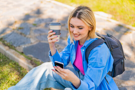 Young pretty blonde woman at outdoors using mobile phone and holding a take away coffee