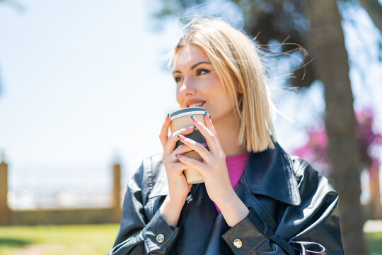 Young pretty blonde woman at outdoors holding a take away coffee