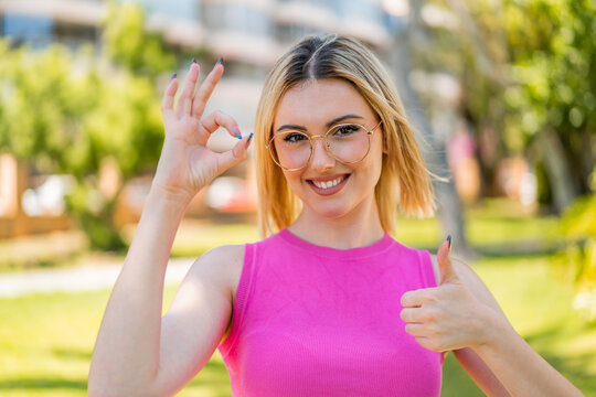 Young pretty blonde woman at outdoors With glasses and doing OK sign