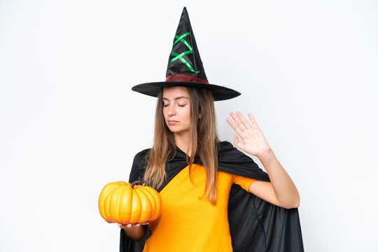 Young caucasian woman costume as witch holding a pumpkin isolated on white background making stop gesture and disappointed