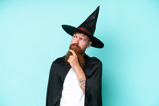 Young wizard in halloween isolated on blue background having doubts and thinking