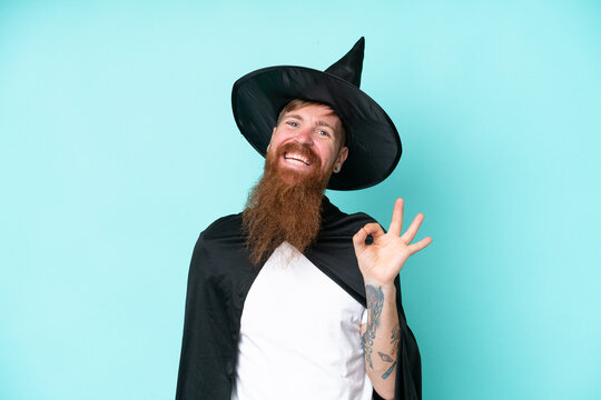 Young wizard in halloween isolated on blue background showing ok sign with fingers