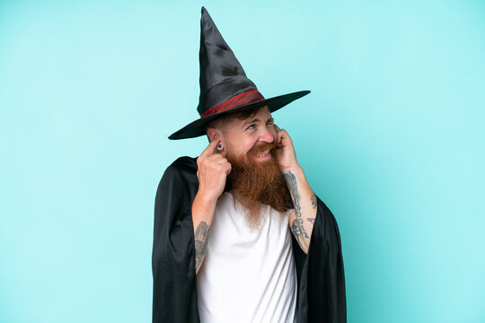 Young wizard in halloween isolated on blue background frustrated and covering ears