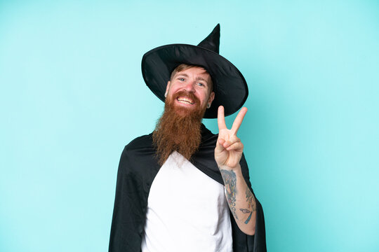 Young wizard in halloween isolated on blue background smiling and showing victory sign
