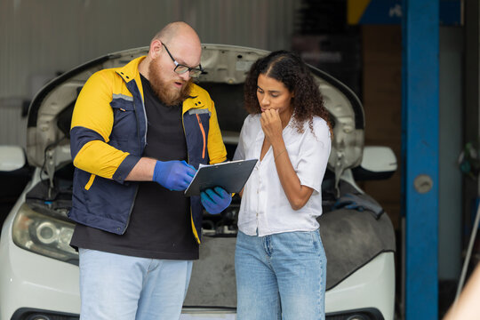 Mechanic checks car engine while customer looks on inside auto repair shop