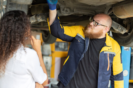 Mechanic checks car engine while customer looks on inside auto repair shop