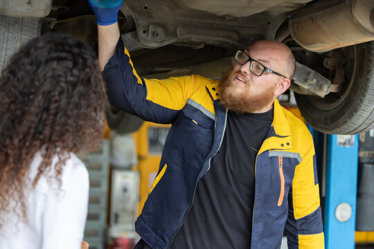 Mechanic checks car engine while customer looks on inside auto repair shop