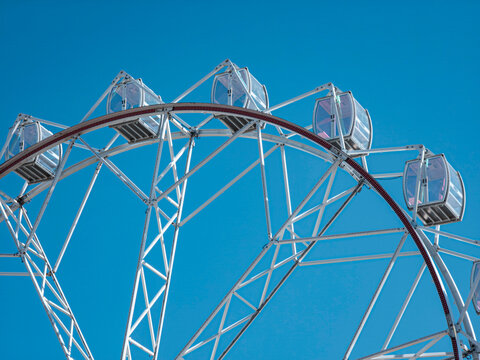 Close up view of a white Ferris wheel frame with glass cabins under a bright blue sky