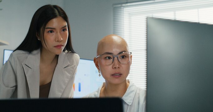 An attractive Asian businesswoman explaining a chart to her colleague indoors. Two diverse entrepreneurs learning, consulting, and analyzing customer data together.
