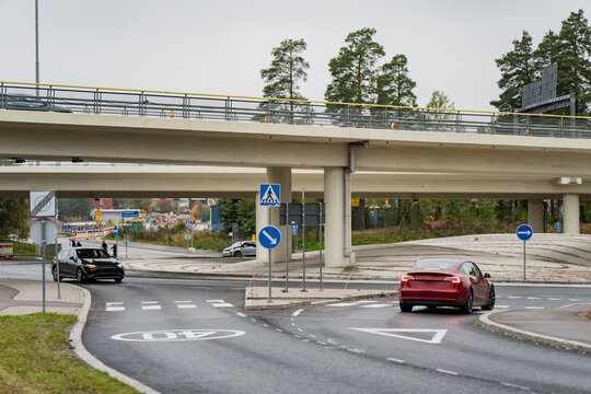 Cars negotiate a road junction beneath concrete flyovers with pedestrian crossings and directional signs, illustrating multilayer transport infrastructure in Finland
