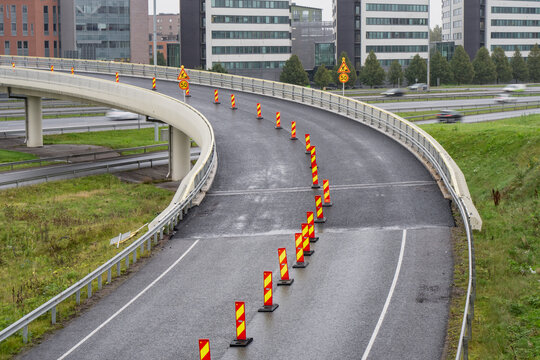 Reflective delineators divide a curved elevated road ramp beside roadwork and speed signs, illustrating temporary traffic control on a Finnish highway interchange