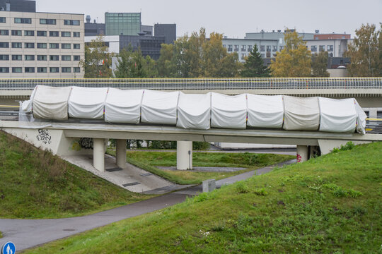 A long covered enclosure spans a concrete road bridge over walking routes in Finland, showing temporary protection around an urban bridge maintenance worksite