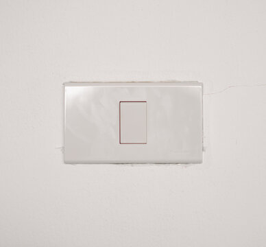 Simple white plastic light switch panel mounted on a white concrete wall