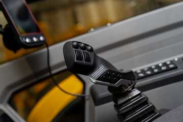 Ergonomic equipment joystick with multiple switches and a flexible base boot inside a cab, representing operator controls for powered construction machinery © K