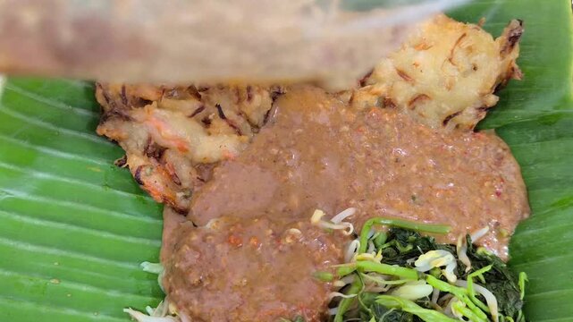 Pouring peanut sauce over traditional Indonesian pecel salad video stock
