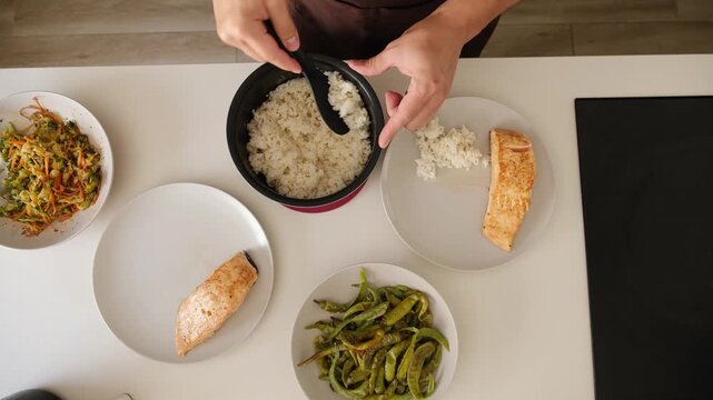 Top down view of a man plating a healthy meal with salmon, rice, and vegetables for dinner