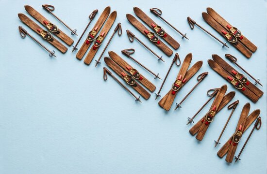 Miniature vintage wooden skis and poles arranged in a diagonal pattern on pale blue with space for winter text