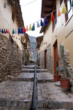 Ollantaytambo cobblestone street with inca water channel and colorful tassels. Peru South America