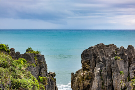 Blick durch geschichtete Kalksteinfelsen auf das t&uuml;rkise Meer bei den Pancake Rocks, Punakaiki, Neuseeland